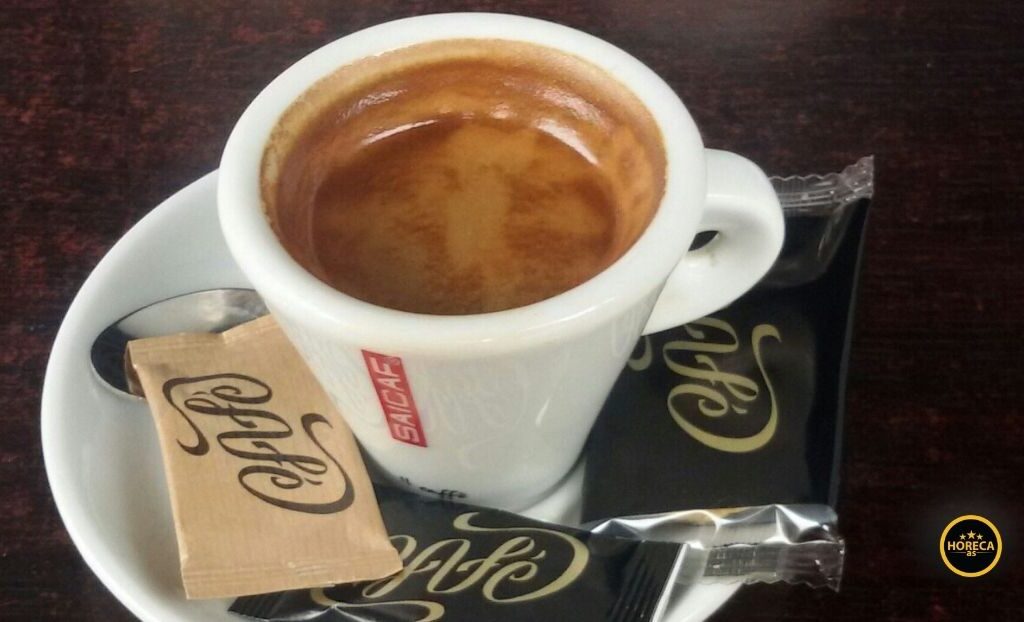 Šoljica espreso kafe sa kesicom šećera i kašičicom na tacni