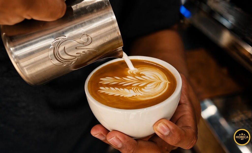 Barista sipa mleko u šoljicu kafe i pravi latte art kao simbol vrhunskog posluženja i premium iskustva