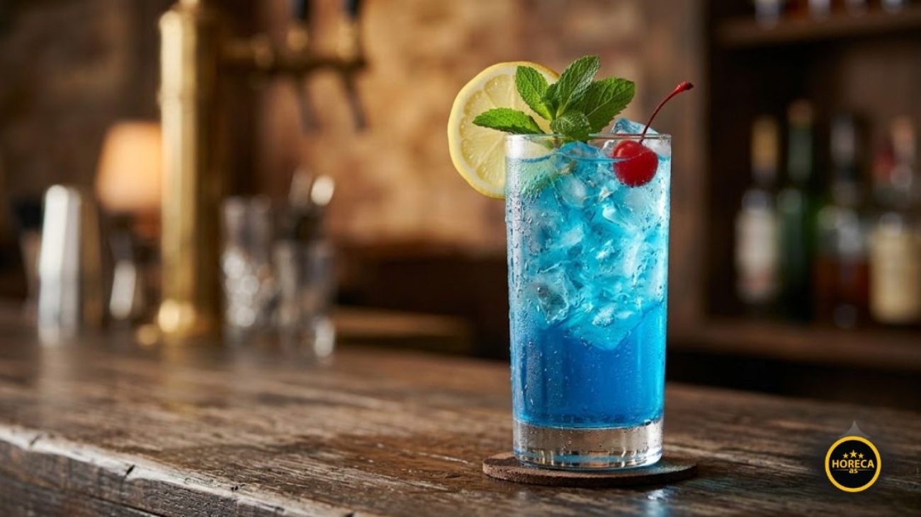 Plavi Blue Lagoon koktel u visokoj čaši sa mnogo leda, dekorisan kriškom limuna, grančicom mente i višnjom, na drvenom baru.