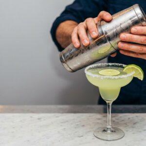 Barmen završava Margarita koktel u čaši sa slanim rubom, ukrašen kriškama limete.