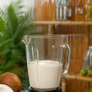 Blender sa belom smesom za Piña Coladu pored svežeg ananasa i kokosa